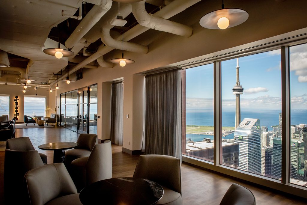 A section of the tenant-exclusive café on the 68th floor, featuring tables and seating options, with a view overlooking downtown Toronto office buildings and the CN Tower.